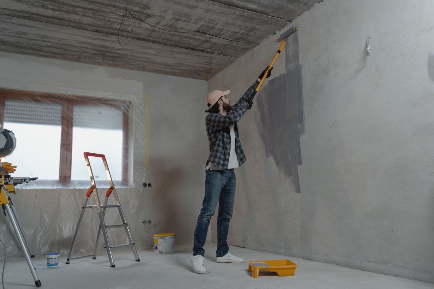 Schilder verft een grijze muur met een verfroller op een lange steel